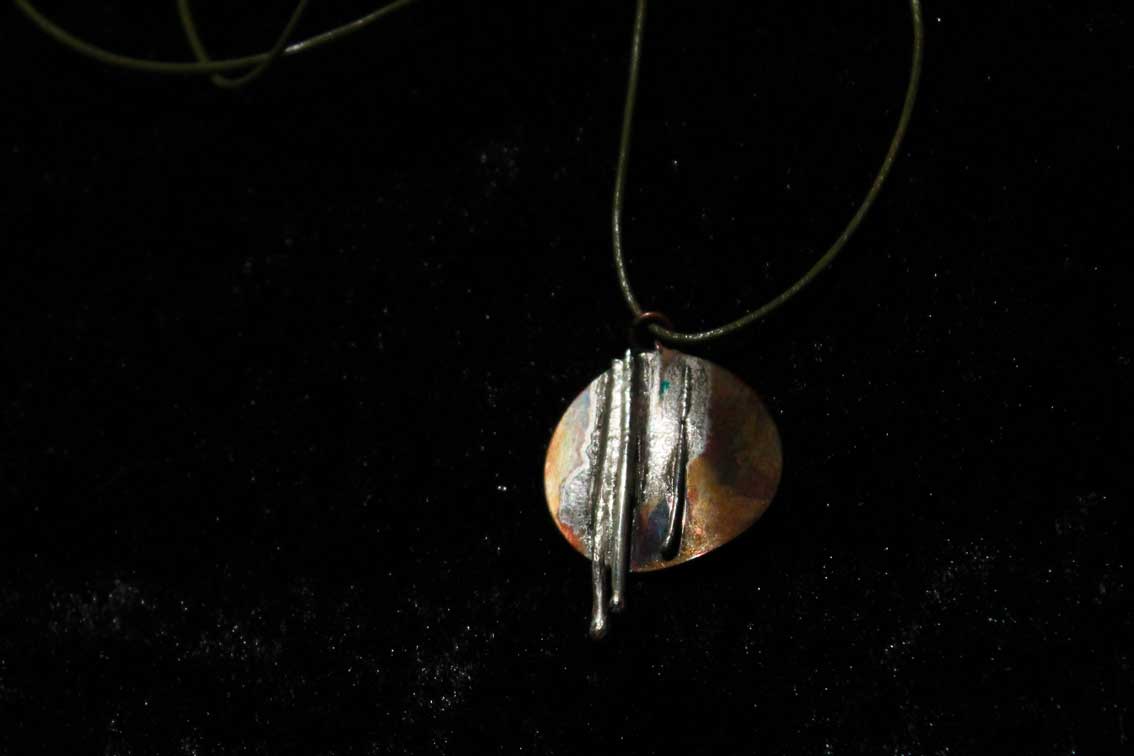 circular copper pendant with three lengths of silver wire fused to it's surface